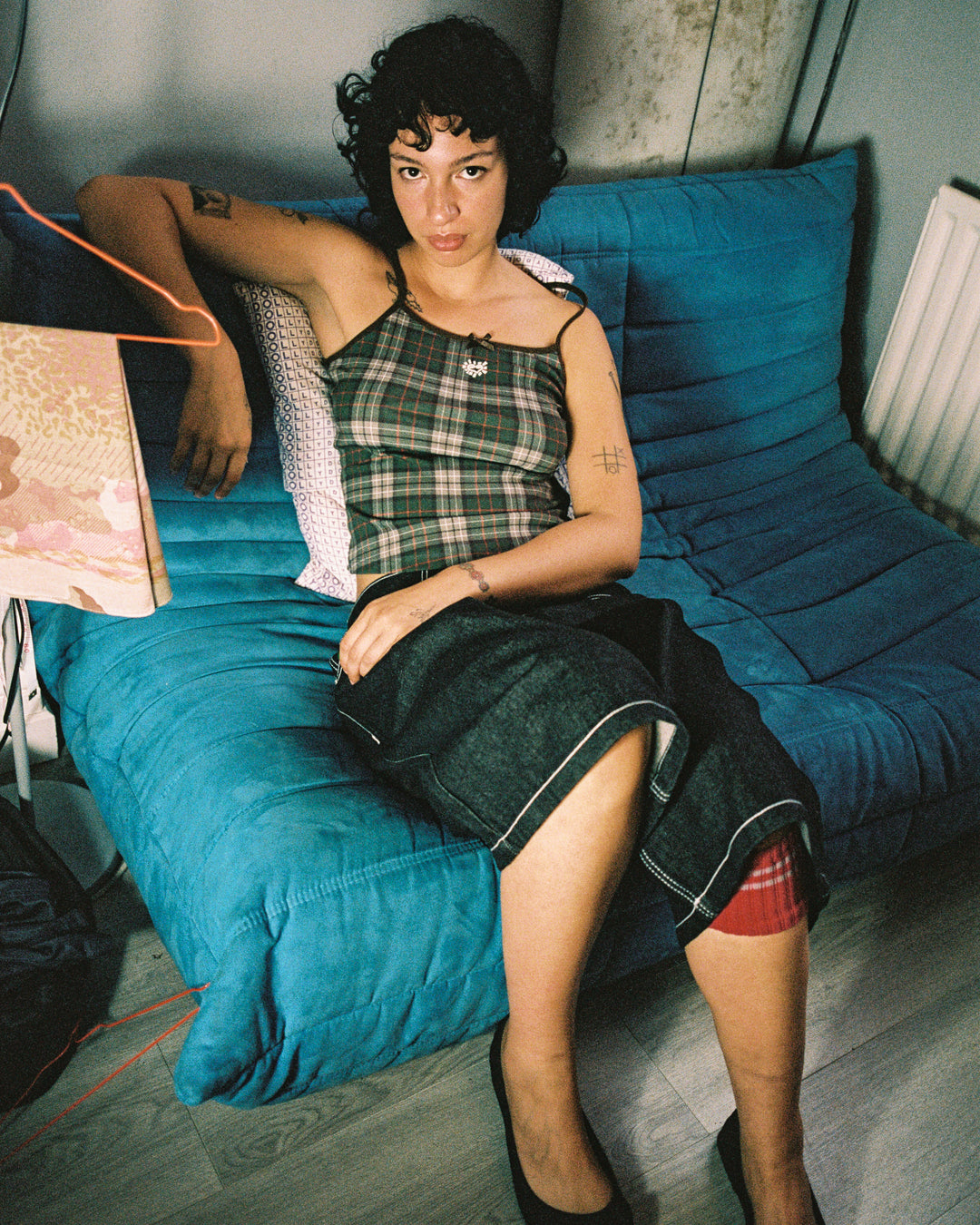 Woman sitting on a blue couch with a plaid dress and red shoes.