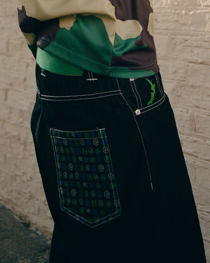 Close-up of black pants with a patterned pocket against a textured wall.