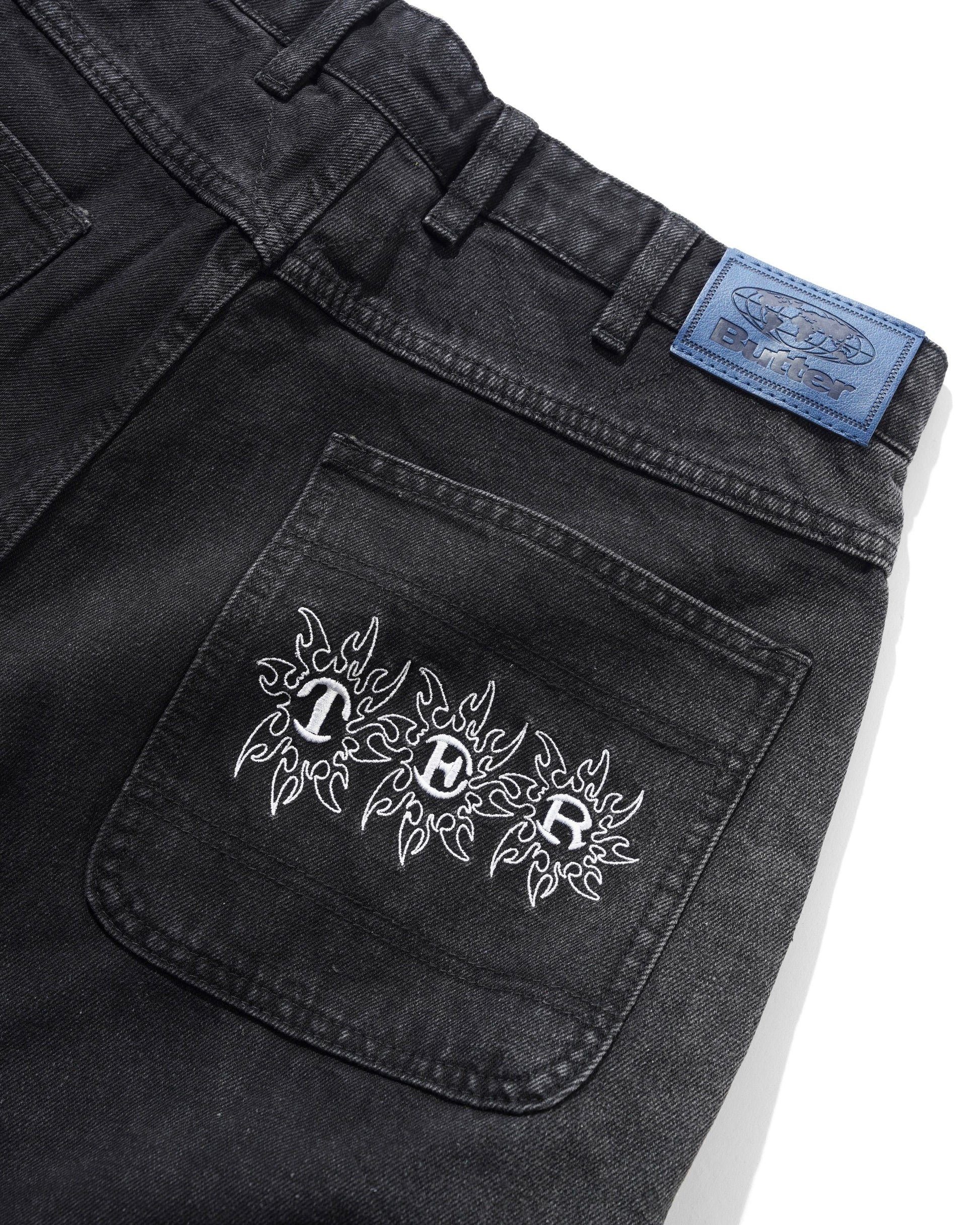 Black denim pocket with white embroidery and a blue label on a white background