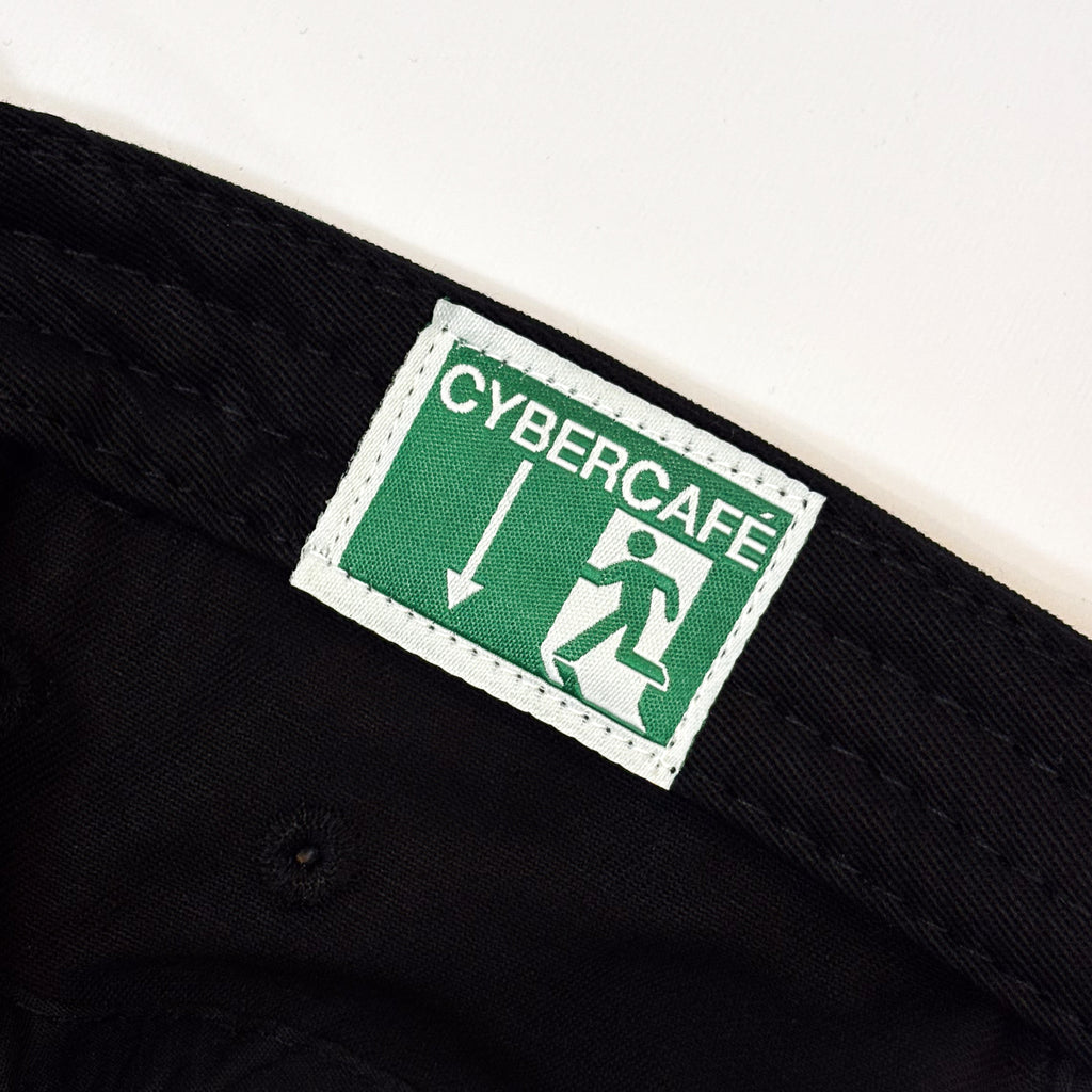 Close-up of a black woven textile item, likely a belt or strap, featuring a rectangular green and white CyberCafe label sewn onto the inside.