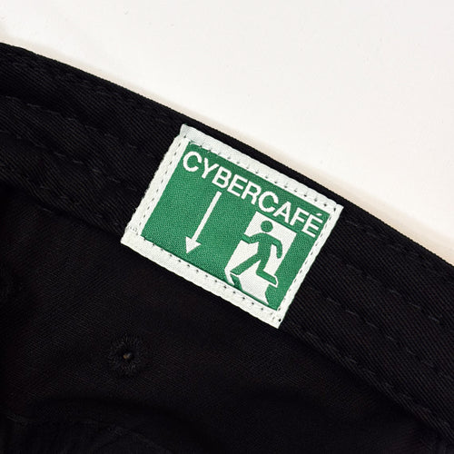 Close-up of a black woven textile item, likely a belt or strap, featuring a rectangular green and white CyberCafe label sewn onto the inside.