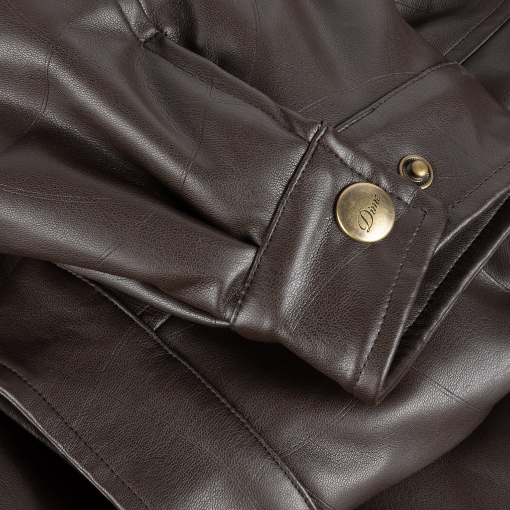 Close-up of a brown leather jacket with a gold button featuring a brand logo.