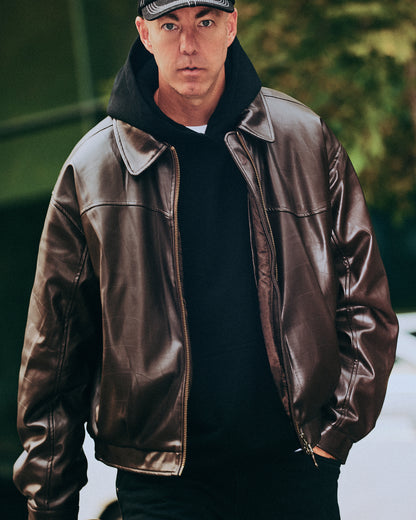 Man wearing a brown leather jacket and black cap outdoors