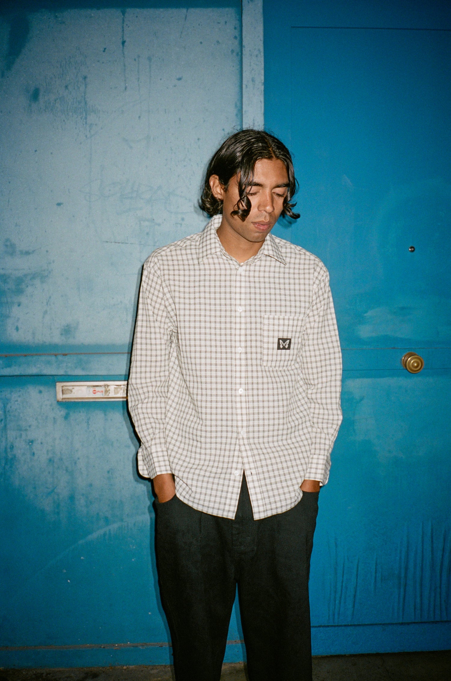 Person wearing a checkered shirt standing against a blue wall.